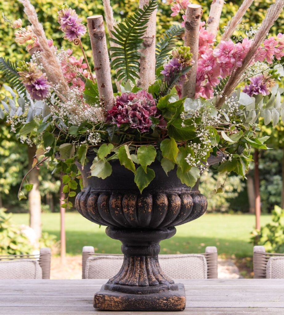 Een foto van een goed gevuld bloemenboeket in een grote vaas op een tuintafel